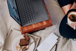 A women working at laptop with a coffee and a slice of cake.
